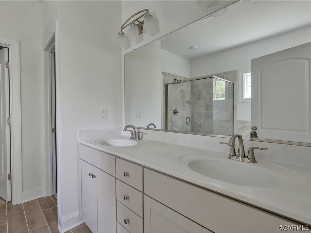 Double-sink bathroom vanity with a wall-length mirror and glass-enclosed tiled shower.
