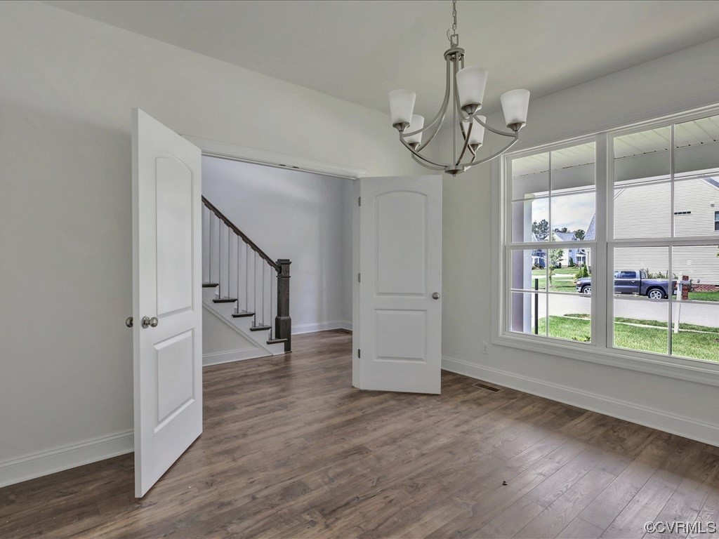 Empty dining room with a chandelier, large windows, and open doors to a staircase.