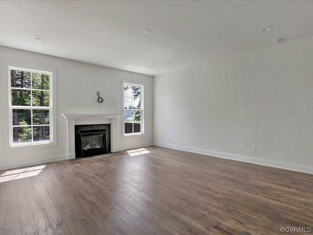 Vacant living room with wood floors, a white fireplace, and windows overlooking trees.