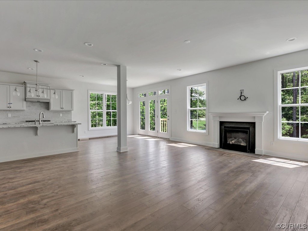 Vacant open-plan living room and kitchen with wood flooring, a fireplace, and large windows.