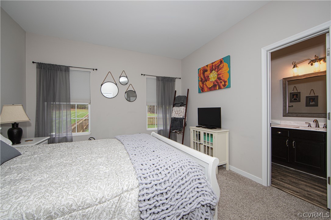 Furnished bedroom with two curtained windows, a white bed, and a doorway to an ensuite bathroom.