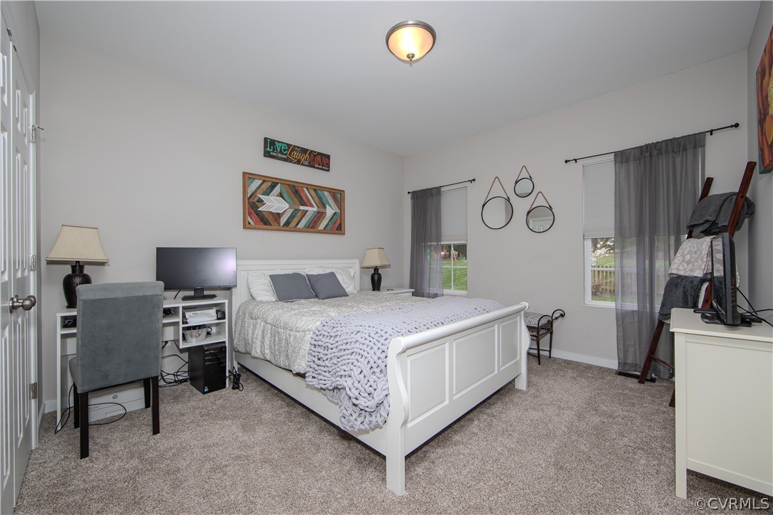 Bedroom with a white bed, chunky knit blanket, gray carpet, and desk by the window.