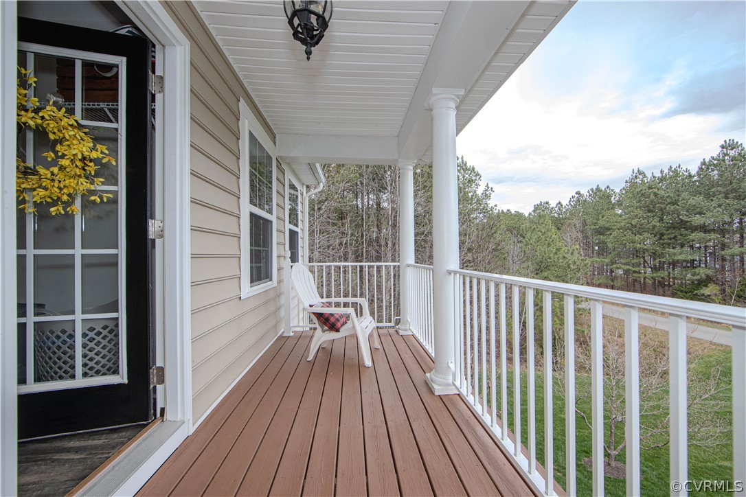 Covered porch with brown decking and a white chair overlooking trees.
