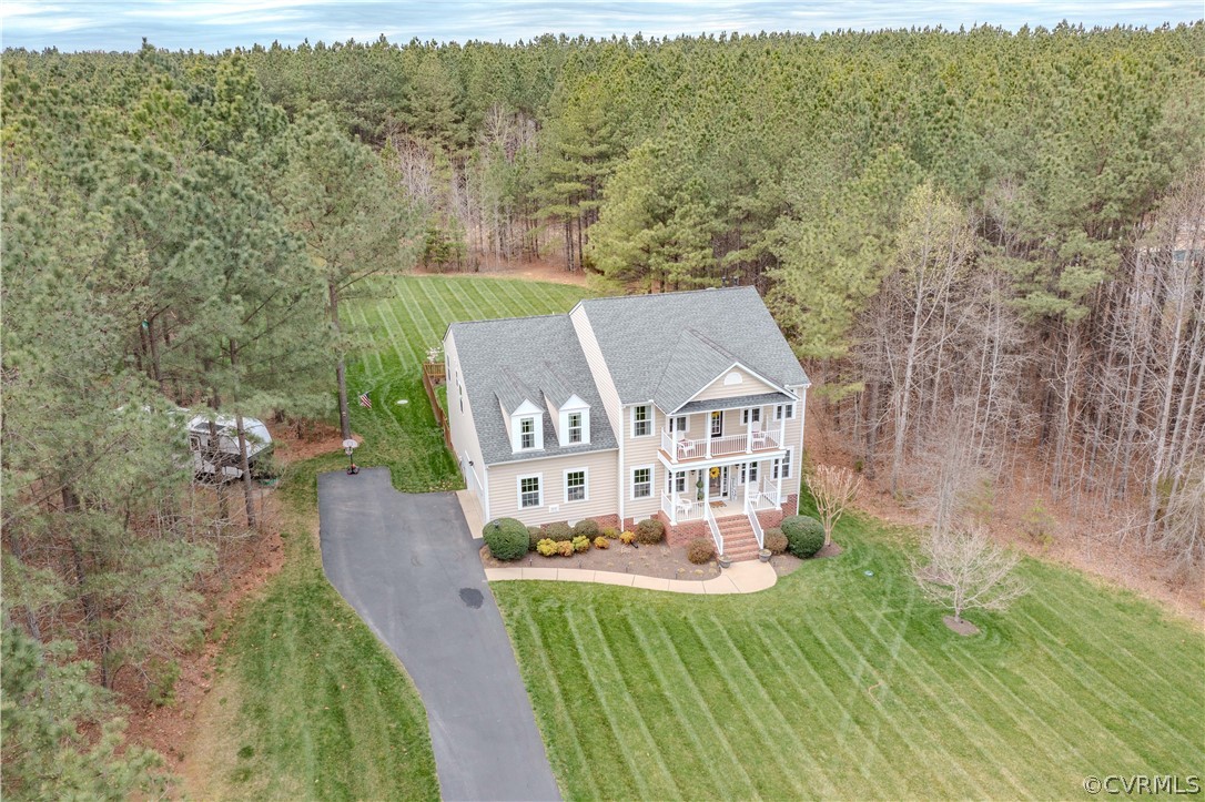Two-story home with front porches, a striped lawn, curved driveway, and surrounding woods.