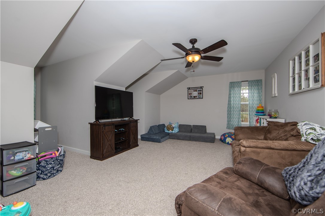 Bonus room with sloped ceilings, a ceiling fan, television, and brown and gray sofas.