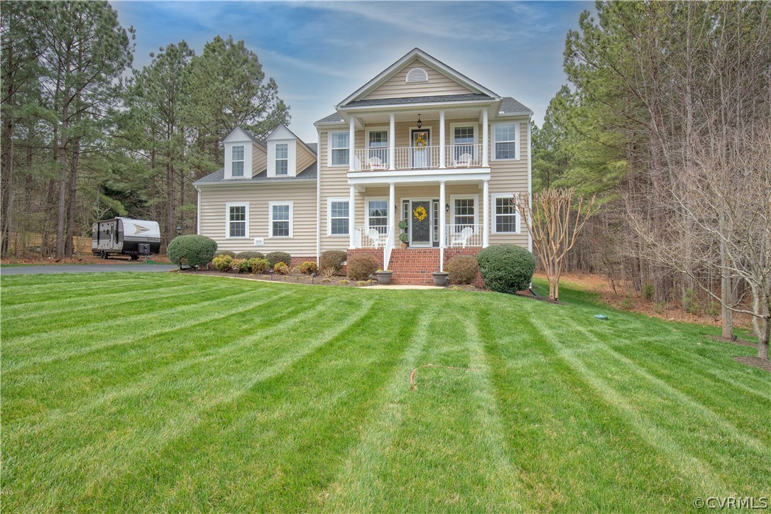 Two-story beige home with stacked porches, brick steps, and a broad striped lawn.