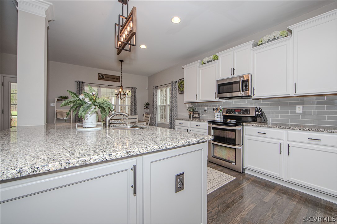 Kitchen with a large granite island, white cabinets, gray tile backsplash, and stainless steel appliances.