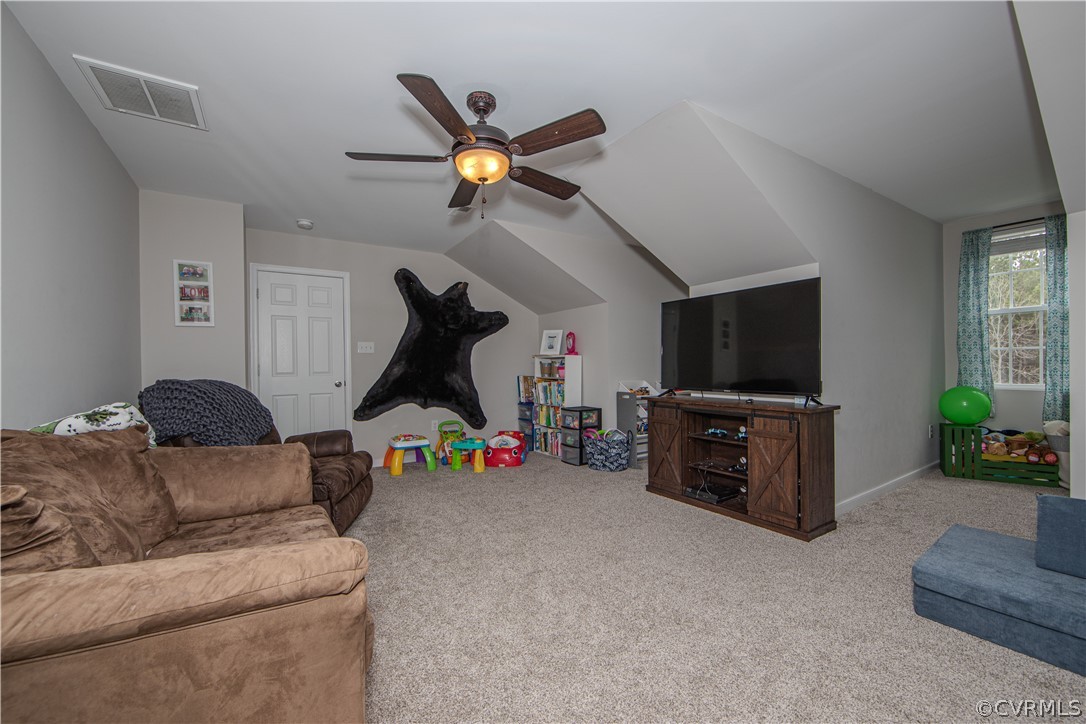Carpeted family room with a vaulted ceiling, ceiling fan, television, brown sofa, and children’s toys.