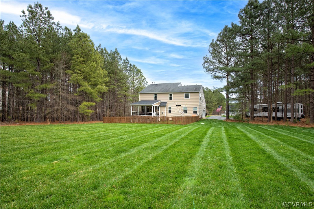 Two-story beige house beyond a broad lawn, with a covered porch, fenced patio, and surrounding pine trees.