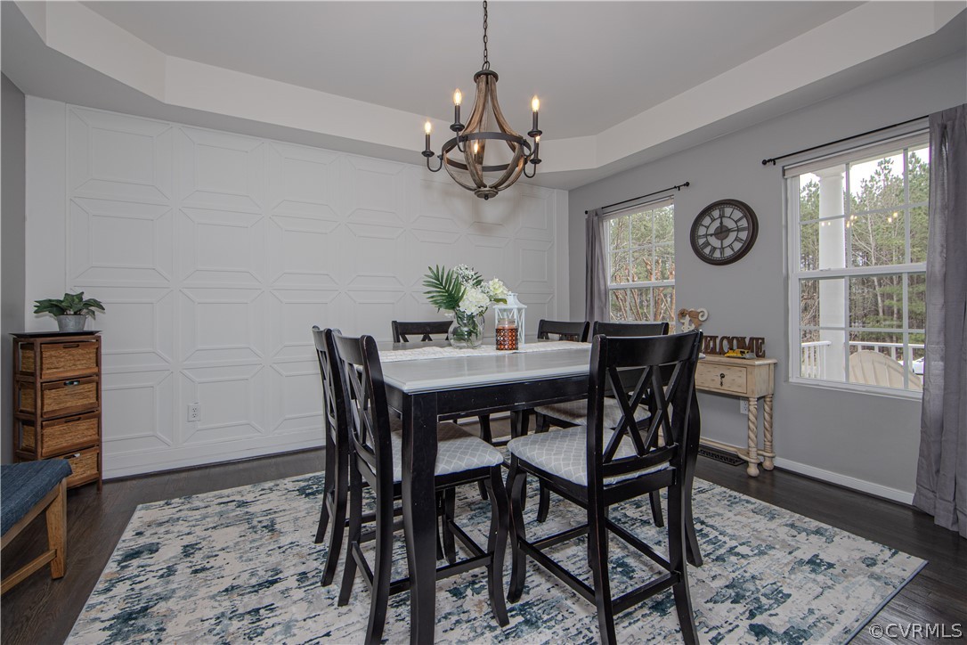 Dining room with geometric wall paneling, a dark table, chandelier, and windows overlooking trees.