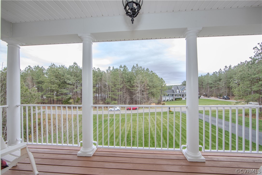Covered porch with white columns overlooking a lawn, neighboring homes, and pine trees.