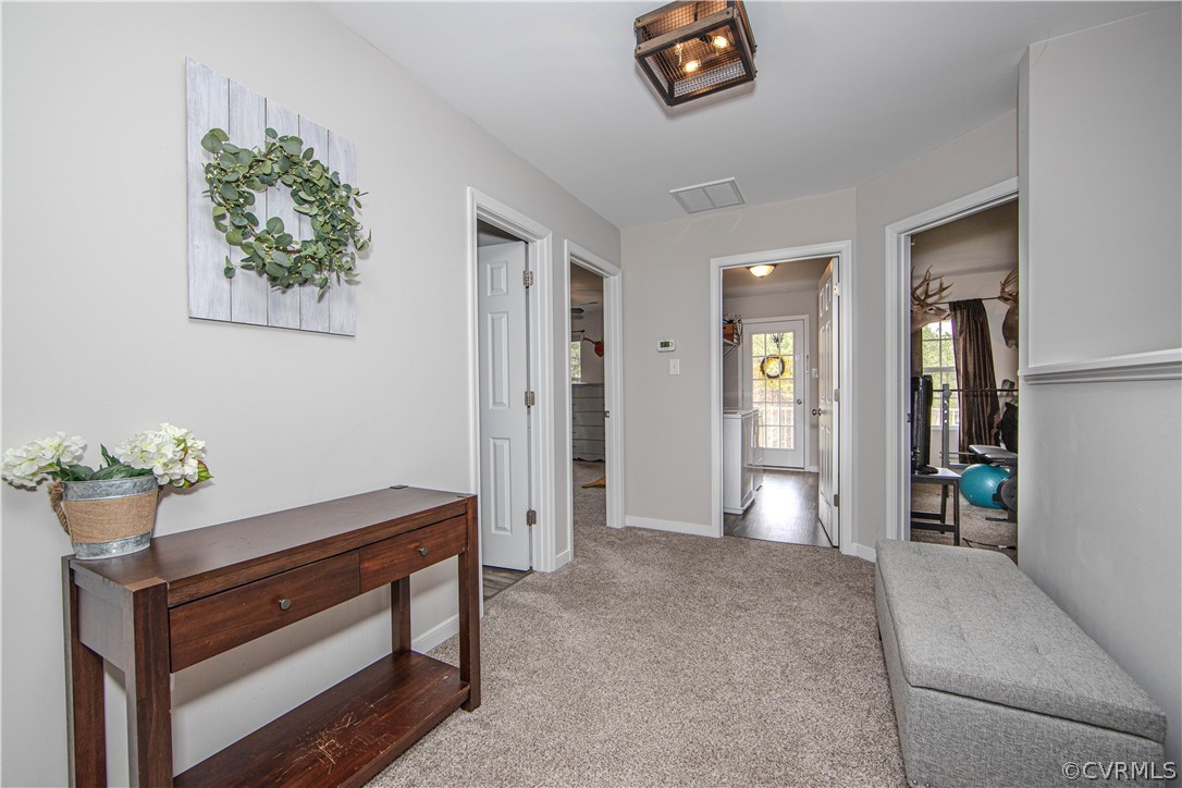 Carpeted hallway with a dark wood console table, gray bench, and open doorways.