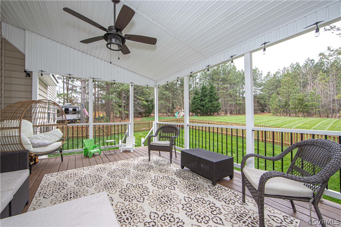 Covered back porch with wicker seating and a ceiling fan overlooking a fenced lawn and woods.