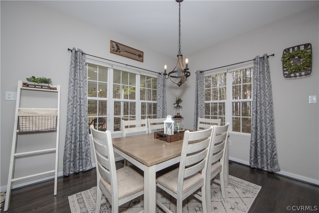 Dining room with a wood-top table, white chairs, and large windows overlooking trees.