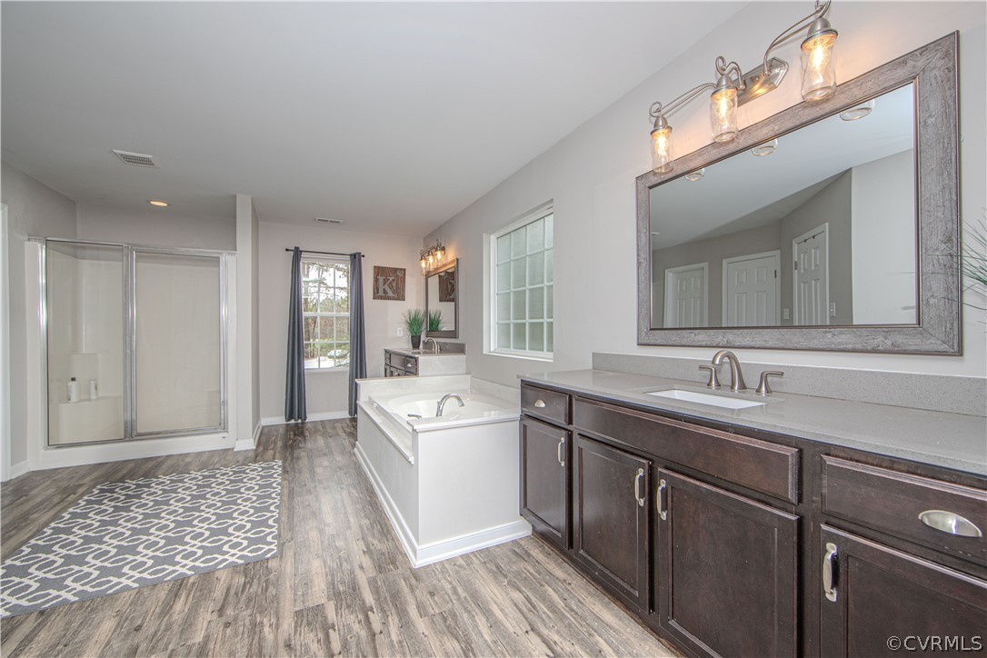 Primary bathroom with a white soaking tub, glass shower, and long dark-wood vanity.