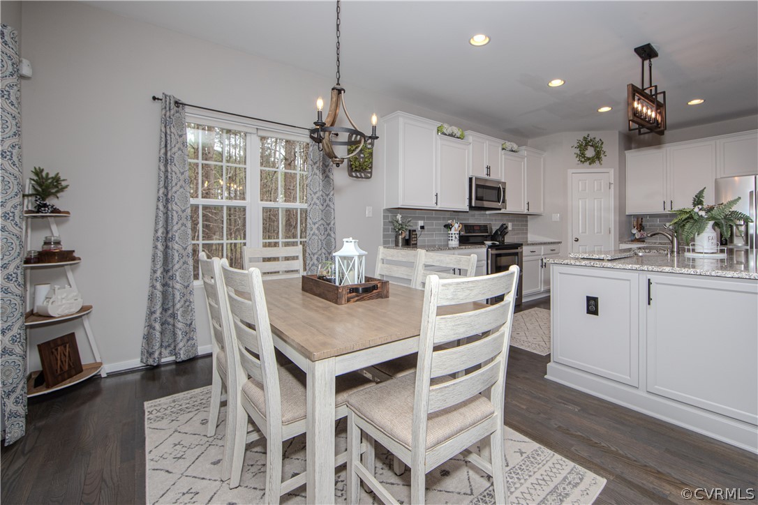 Dining area with a light wood table and white chairs beside a bright kitchen with granite counters.