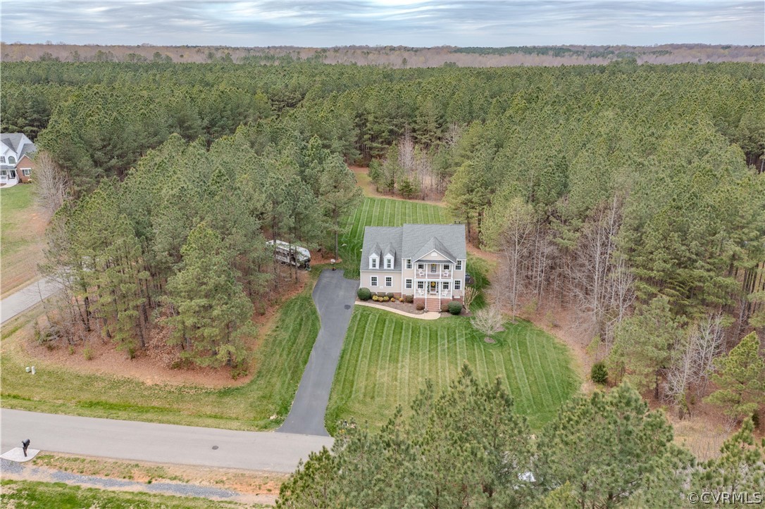 Aerial view of a two-story home with a broad striped lawn and surrounding woods.