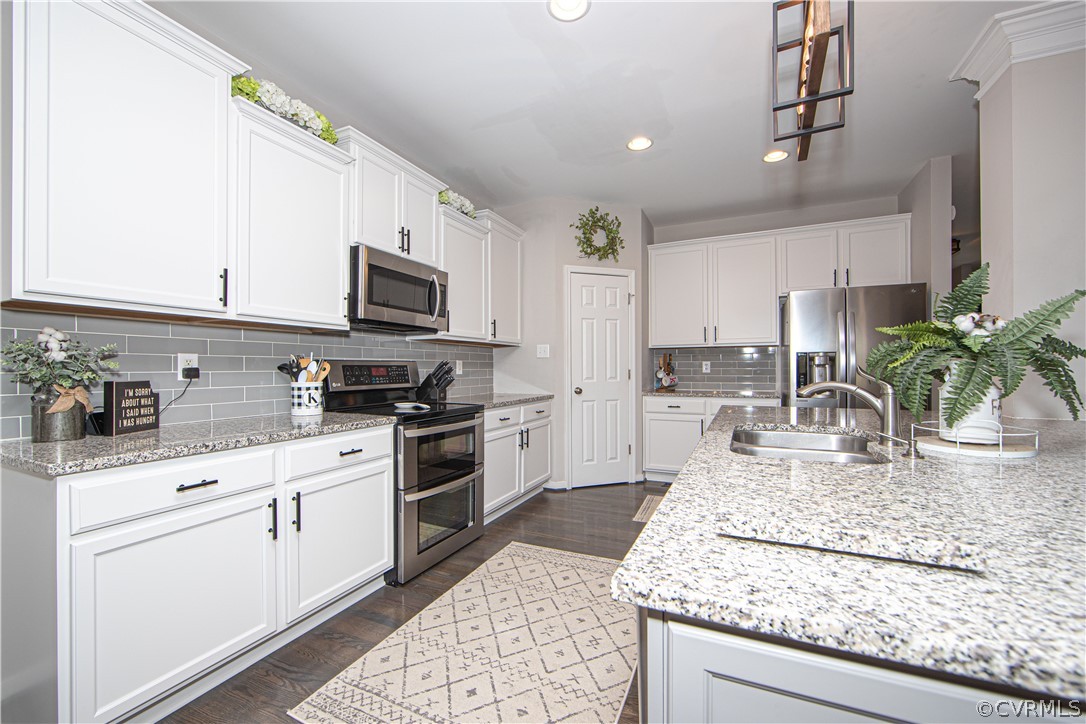 Kitchen with white cabinets, granite counters, stainless steel appliances, and a large island with a double sink.