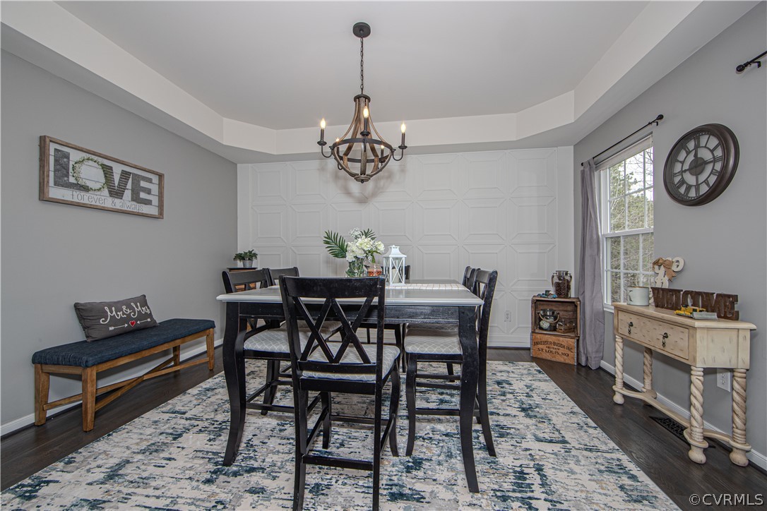 Dining room with a dark wood table, patterned rug, geometric paneled wall, and chandelier.