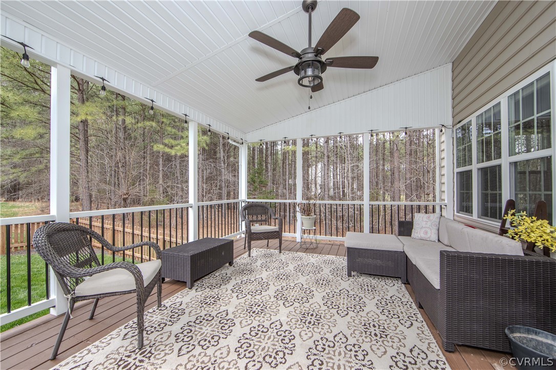 Covered porch with wicker seating, a ceiling fan, and woods beyond the railing.