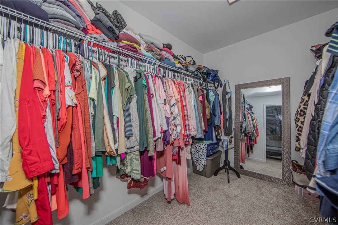 Walk-in closet packed with colorful clothes, high shelves, and a full-length mirror.