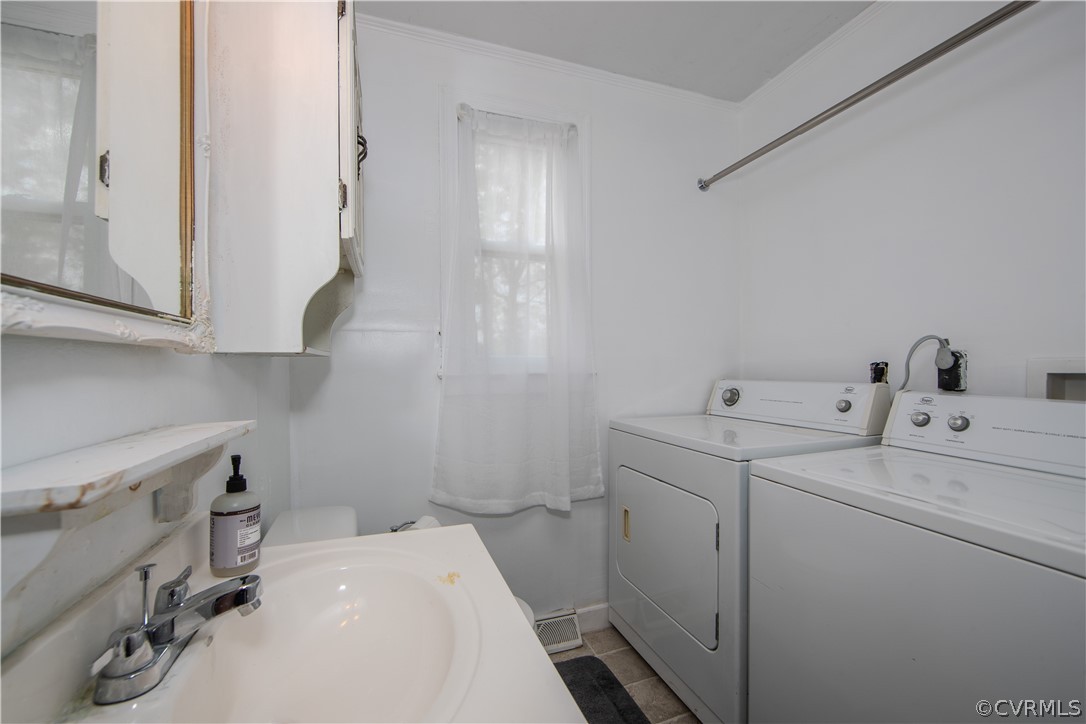 Laundry room with white washer and dryer beside a sink vanity and curtained window.