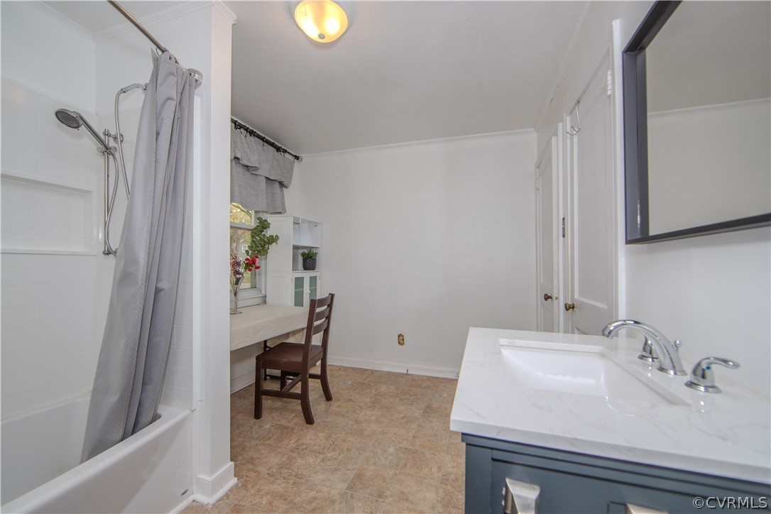 Bathroom with a tub, gray shower curtain, white sink countertop, and vanity desk beside a window.