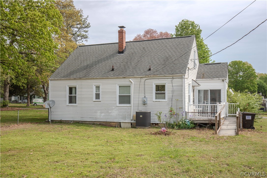 Rear of a light-colored house with a brick chimney, raised deck, and wooden ramp.