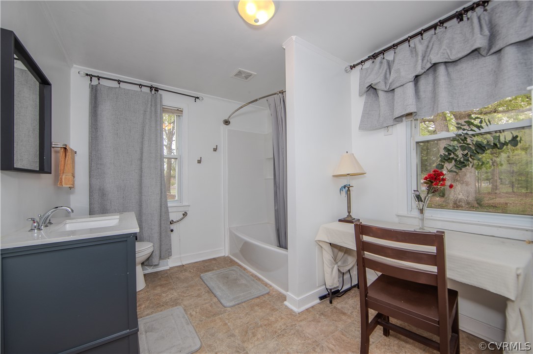 Bathroom with a dark blue vanity, gray-curtained bathtub, and window overlooking trees.
