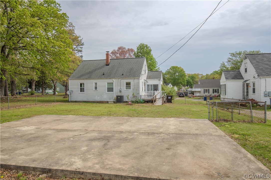 Single-story white house with a small deck behind a broad concrete slab and fenced yard.