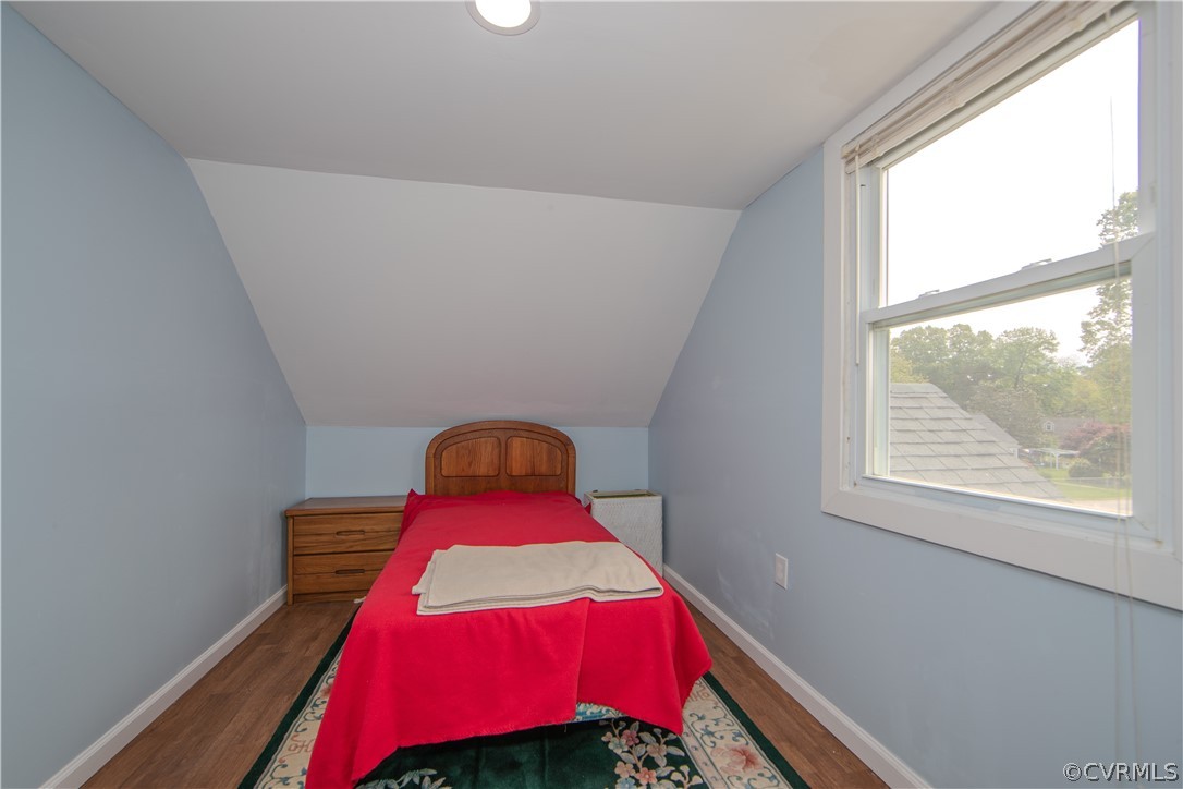Bedroom with a red-covered single bed, sloped ceiling, and large window overlooking trees.