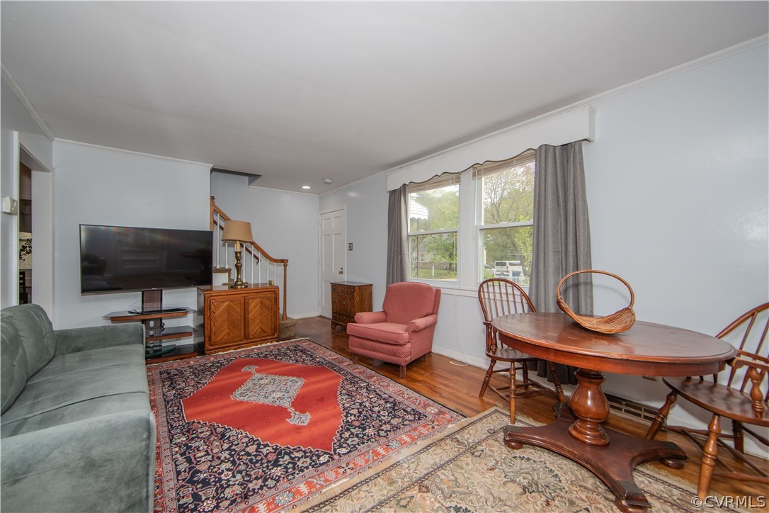 Living and dining room with hardwood floors, a red patterned rug, and a wooden oval dining table.
