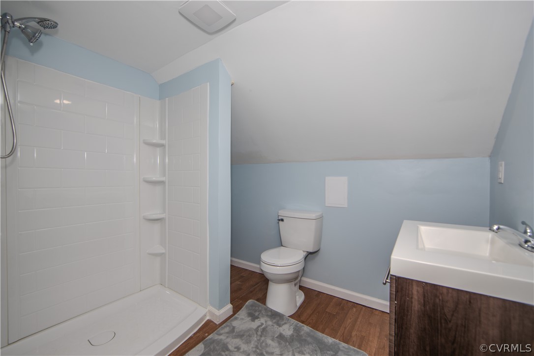 Bathroom with a white tiled shower, toilet, and dark wood vanity against light blue walls.