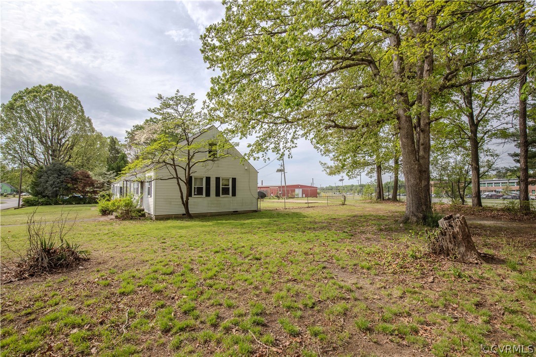 Single-story house in a grassy yard beneath mature trees, viewed from the side.