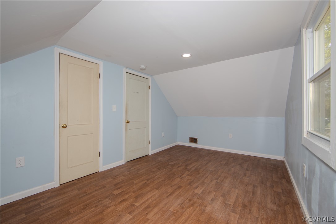 Empty upstairs room with a sloped ceiling, blue walls, and brown wood-look flooring.