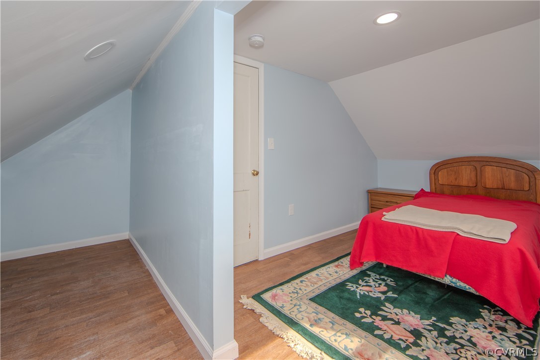 Attic bedroom with a red-covered bed, sloped ceiling, and floral rug.