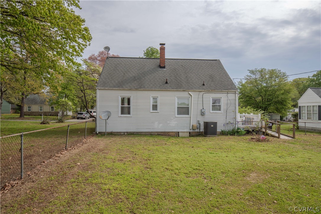 Rear of a light-sided house with a brick chimney, small deck, and fenced grassy yard.