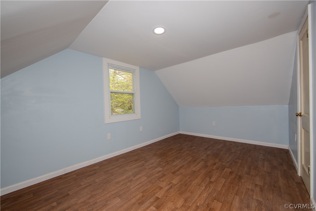 Vacant attic bedroom with pale blue walls, sloped ceilings, and brown wood-look flooring.