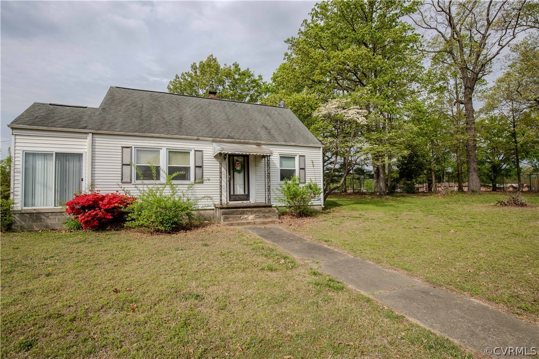 Single-story house with a covered front entry, broad lawn, mature trees, and flowering shrubs.