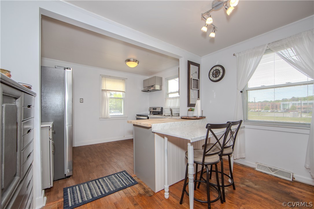 Kitchen with a marble-look breakfast bar, two stools, stainless-steel refrigerator, and wood floors.