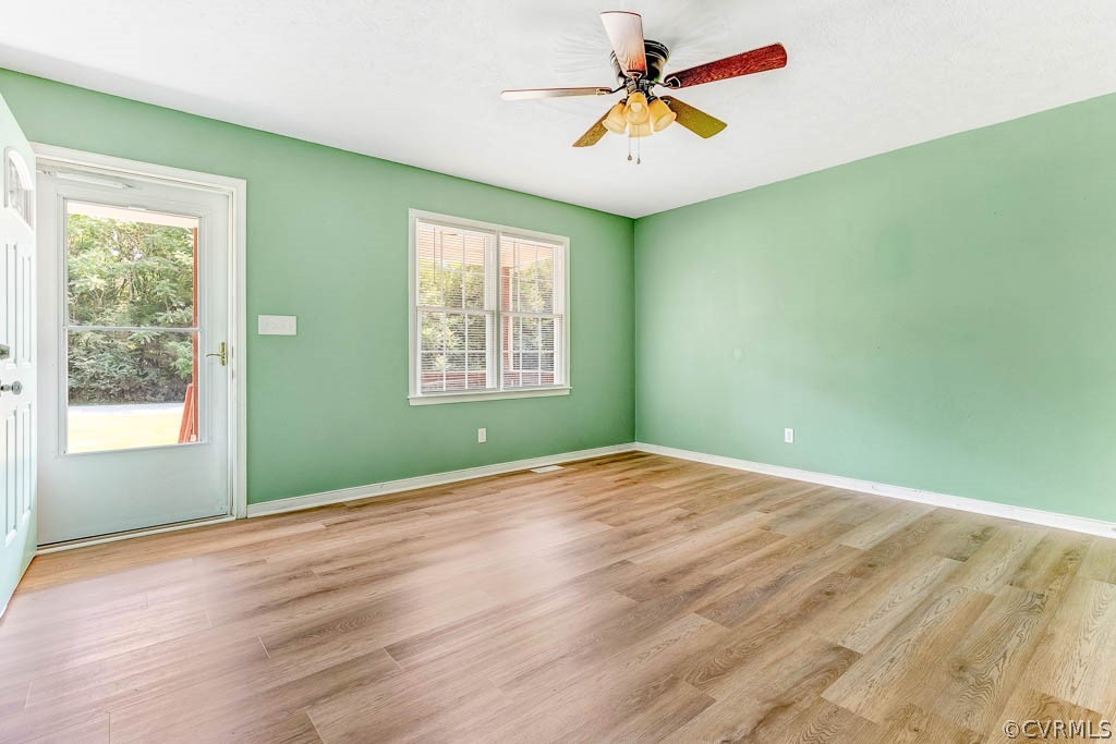 Empty green room with wood-look floors, ceiling fan, and glass-paneled door opening to greenery.