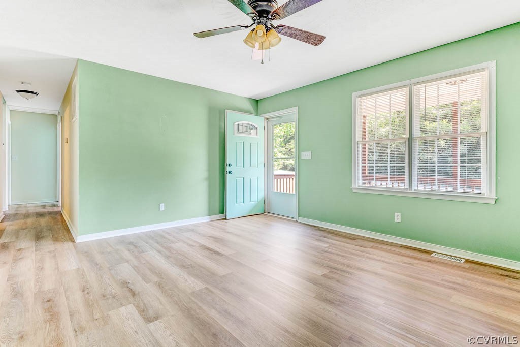Empty room with pale green walls, light wood-look flooring, ceiling fan, and a window beside the exterior door.