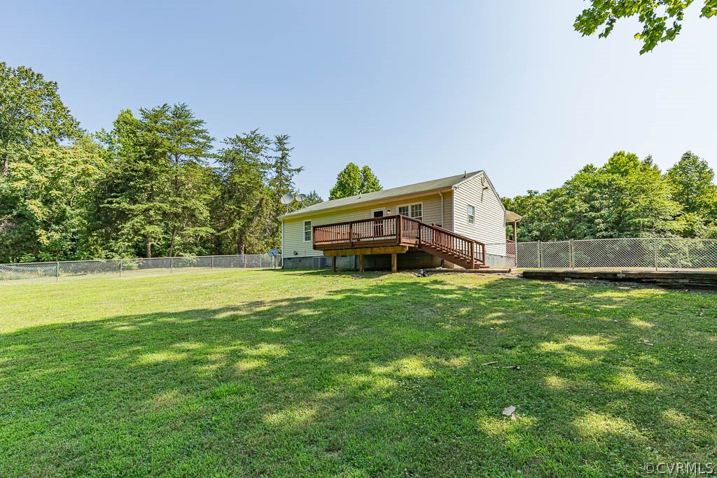 Rear of a single-story home with a raised wooden deck overlooking a fenced lawn.