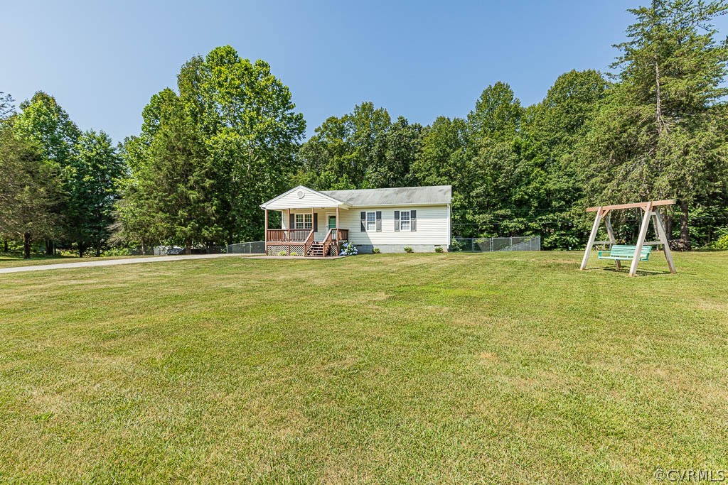 Single-story house beyond a broad lawn, with a small deck and a green bench swing.