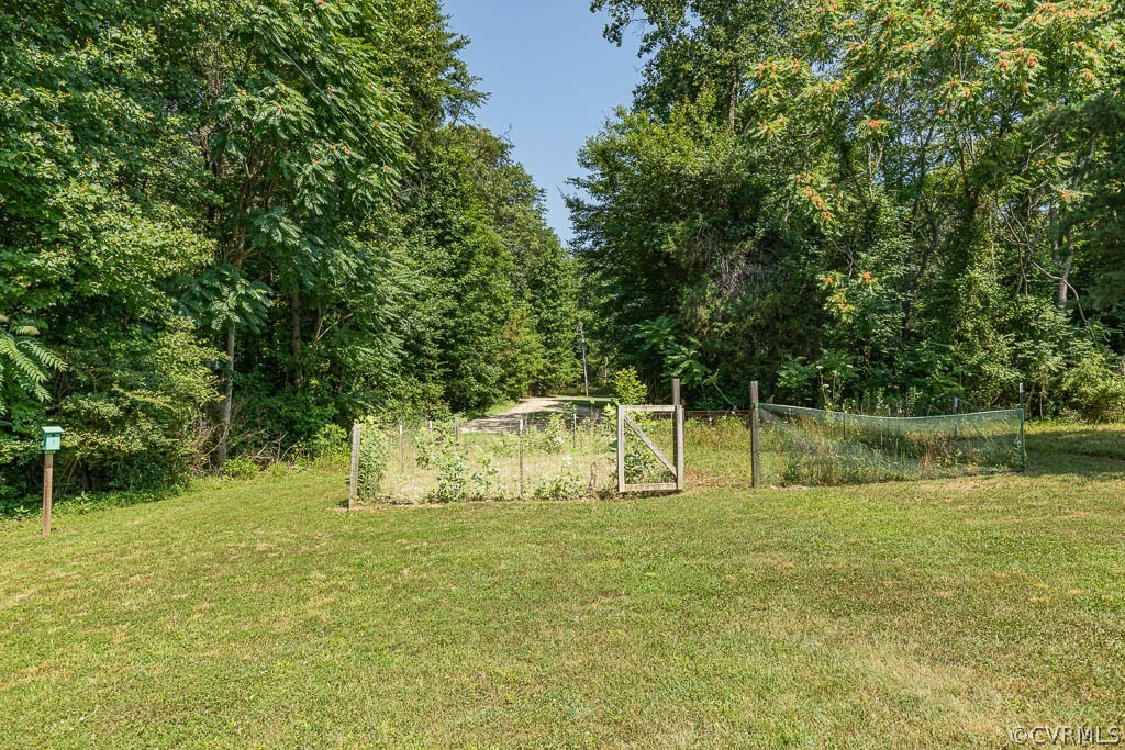 Fenced garden plot with a wooden gate sits beyond a broad lawn, backed by mature trees.