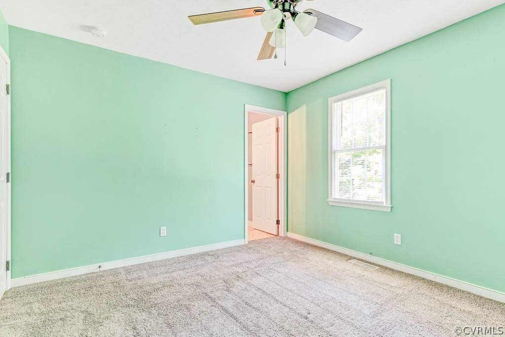 Empty mint-green bedroom with carpet, ceiling fan, and a window with white blinds.