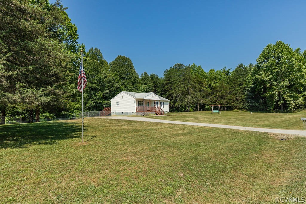 White single-story home beyond a broad lawn, with a flagpole, driveway, mature trees, and swing set.