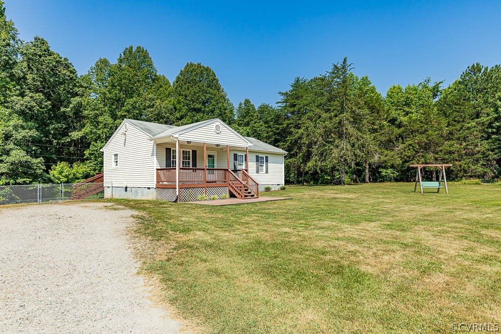 White house with a covered porch, gravel driveway, grassy yard, and swing set.