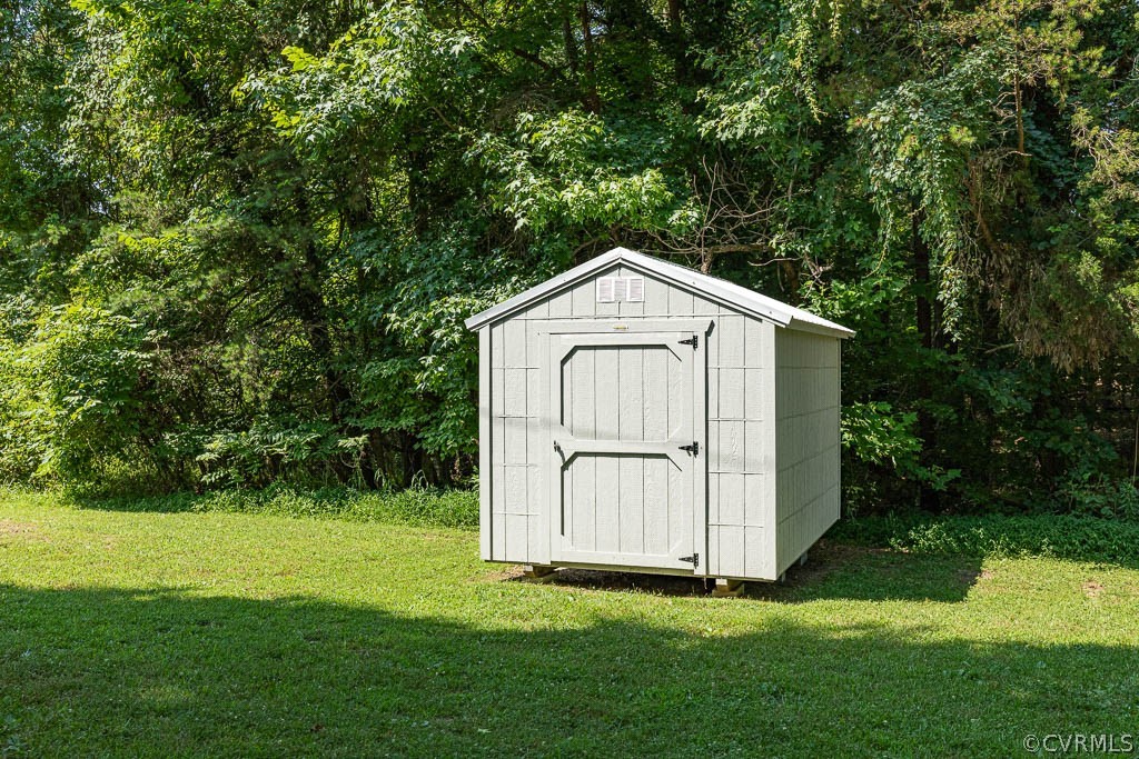 Light gray storage shed with double doors on a lawn beside dense trees.
