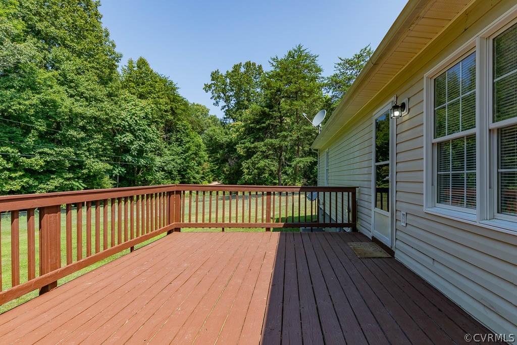 Wooden deck beside a light-colored house, overlooking a grassy yard and dense trees.
